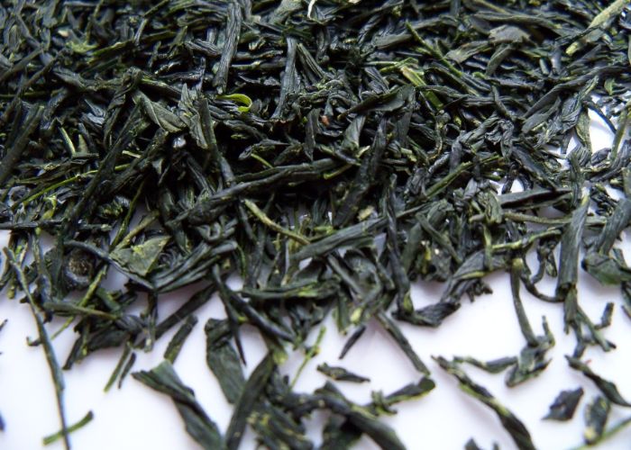 A close up image of vivid dark green rolled gyokuro tea leaves on a white background