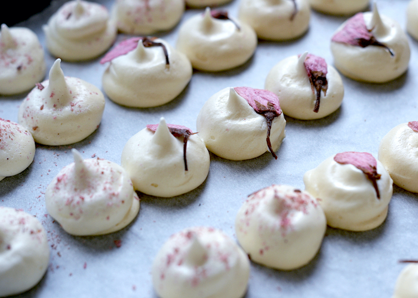 Kiss-shaped sakura meringues arranged on a baking tray