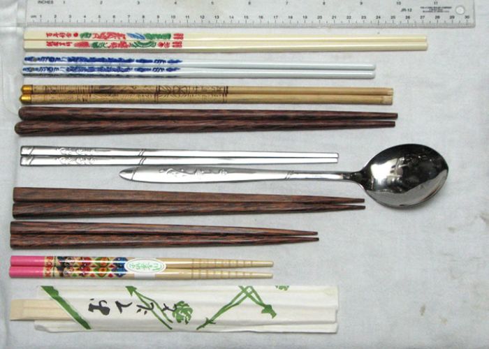 An overhead image of nine different pairs of chopsticks lined up next to a ruler
