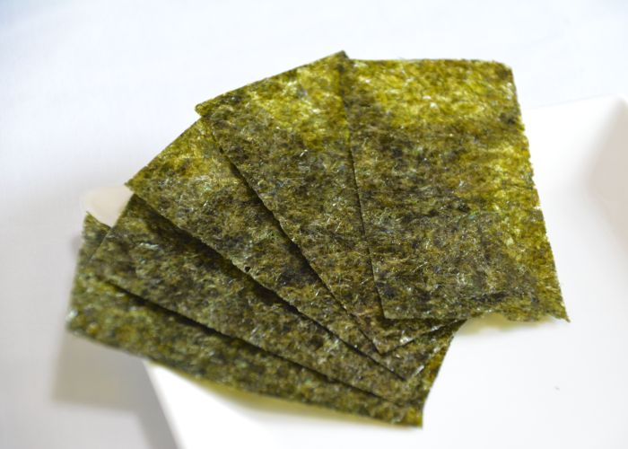 Five thin green sheets of nori seaweed fanned out on a white plate