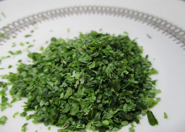 A pile of green aonori seaweed flakes on a white background