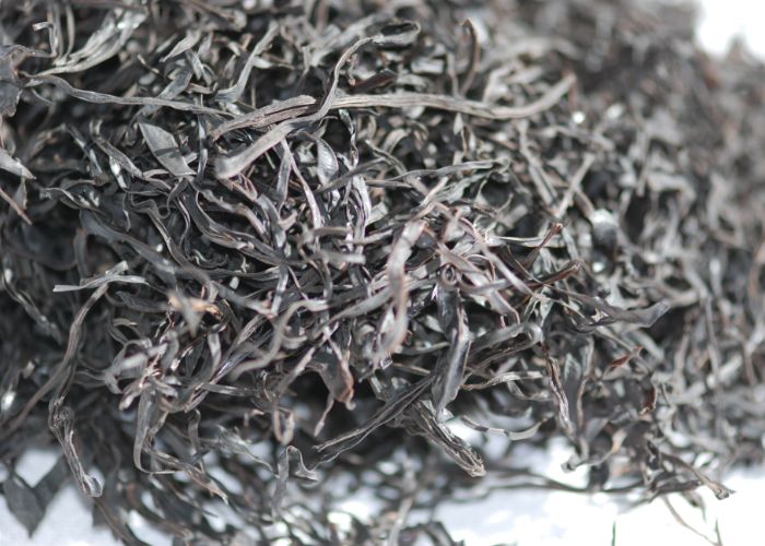 A close up image of a pile of dried, thin dark brown strands of arame seaweed