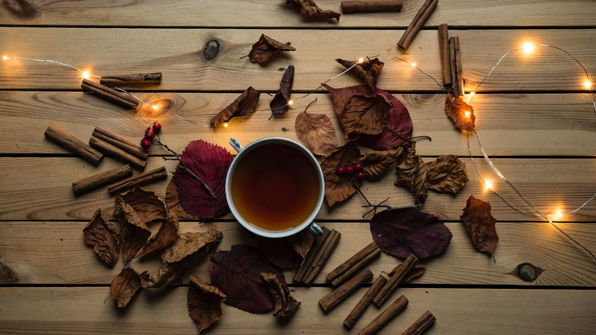 Warm cup of tea with autumn leaves and cinnamon sticks on wooden table