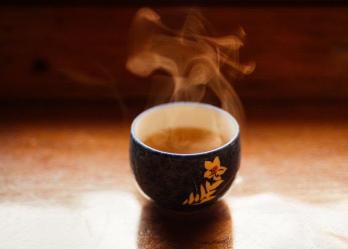 A small ceramic teacup filled with light brown tea, with steam rising from the surface