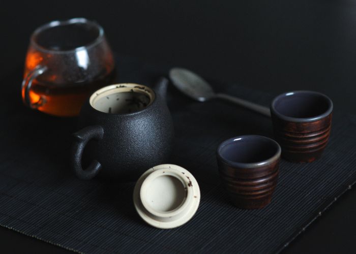 A tea set with a black teapot, glass teapot, and two brown teacups against a dark background