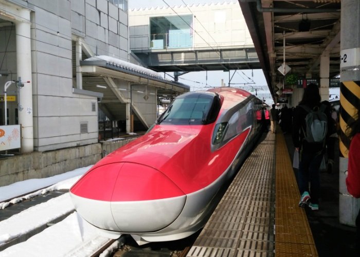 Red nosed shinkansen fast train pulling up in Akita in winter