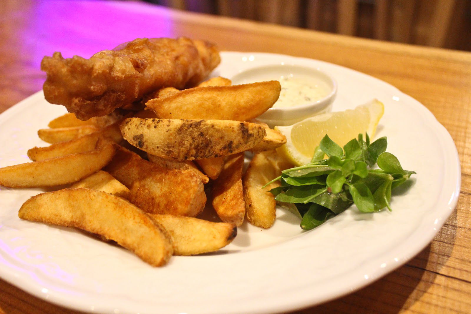 Fish and chips with tartar sauce on a white plate in a cozy restaurant.