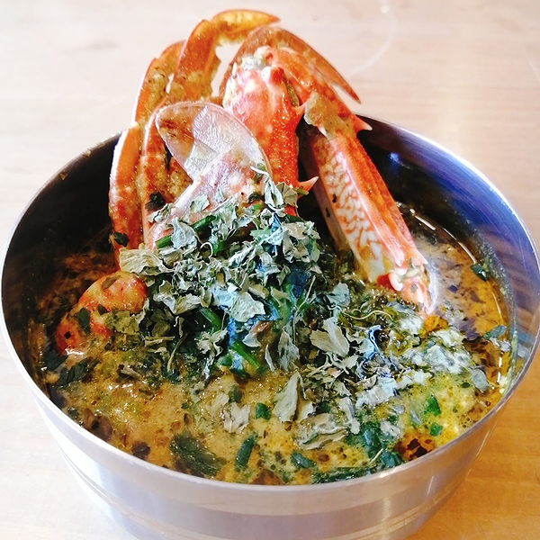 Spicy crab curry garnished with herbs in a steel bowl