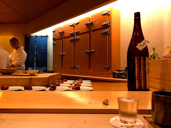 Sushi bar interior with chefs and sake bottle on counter