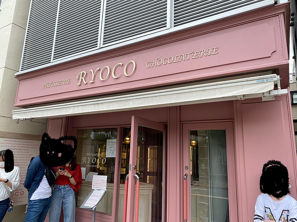 Chic patisserie storefront with pink facade and waiting patrons