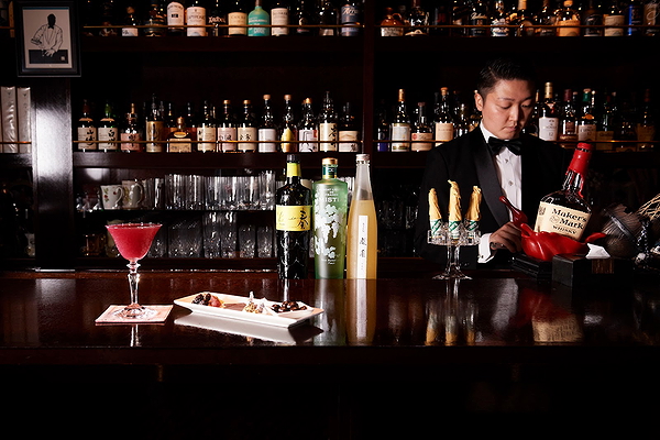 Elegant bar with bottles, cocktail, and bartender in tuxedo