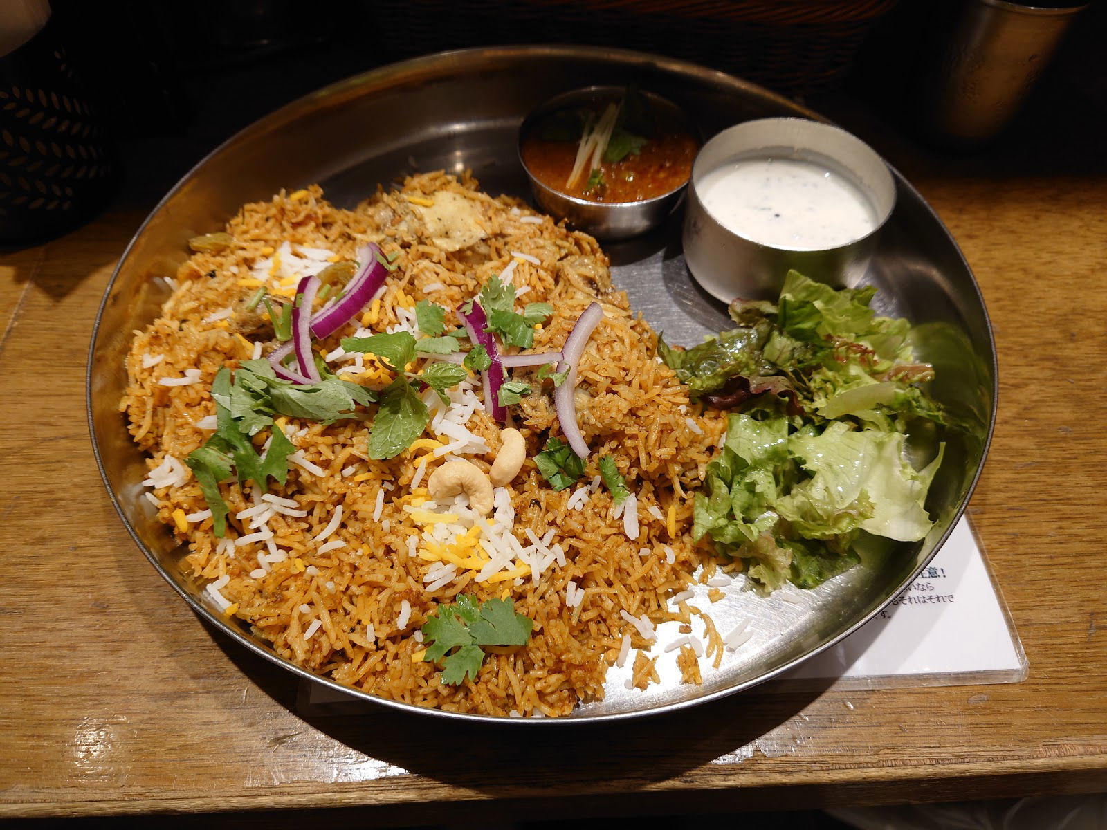 Plate of flavorful biryani with salad and sauces on a wooden table