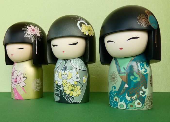Three kokeshi dolls in a row against a green background