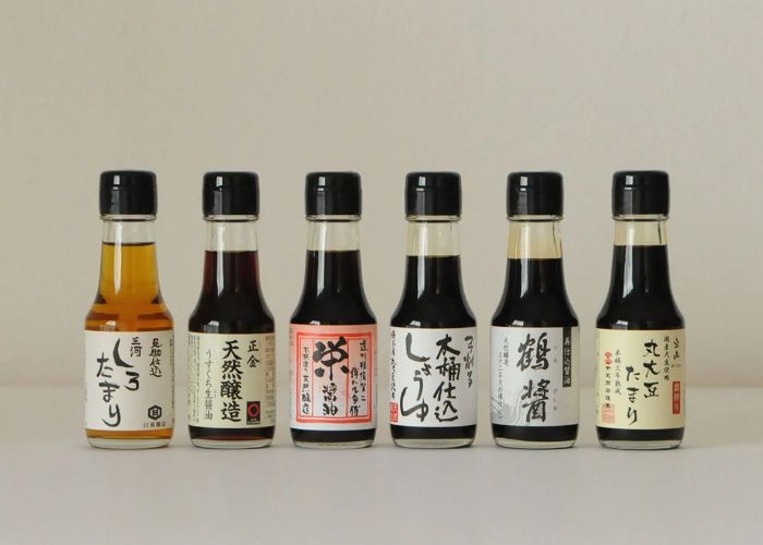 Six mini bottles of dark brown soy sauce in a row