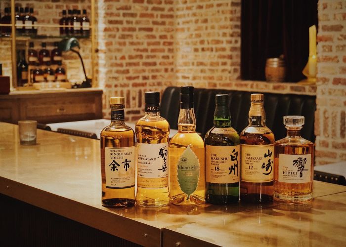 Six different bottles of Japanese whisky lined up on a bar with a brick wall in the background