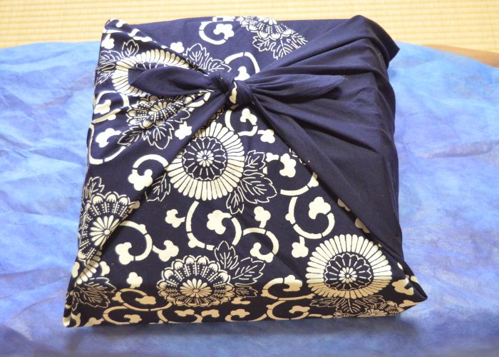 A gift wrapped in a dark blue furoshiki wrapping cloth with gold detailing