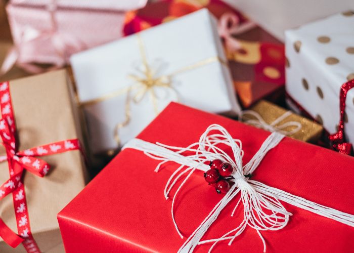 A bundle of Christmas gifts, with a red box tied with thin white ribbon in the foreground