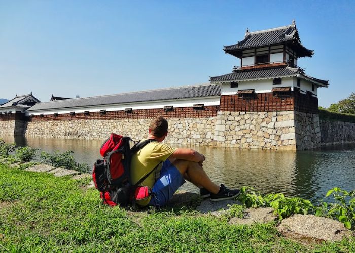 A backpacker rests near the water-filled moat of one of Japan's historical castles.