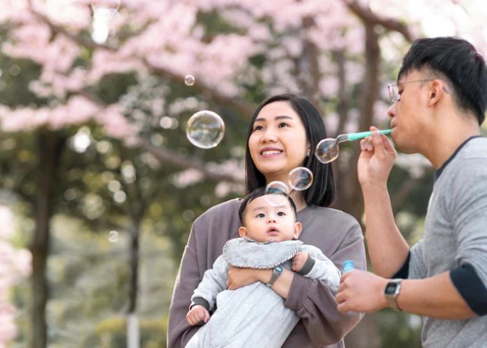 A Japanese couple with a baby enjoy blowing bubbles. Spending time outside is a fun activity in Japan for families