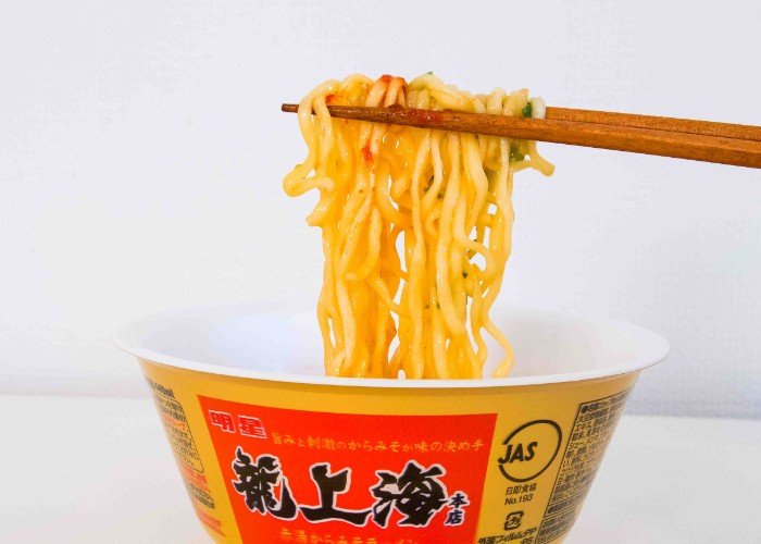 chopsticks lifting noodles out of a bowl of instant noodles.