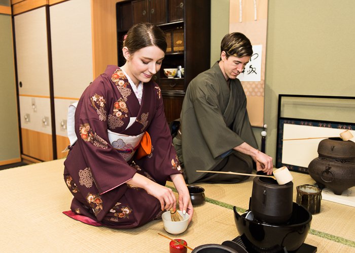 A couple in kimono whisk bowls of matcha in a traditional Japanese room
