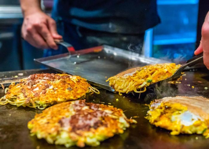 Four okonomiyaki pancakes being cooked on a hot plate