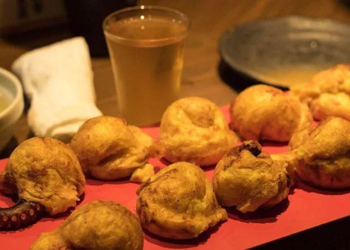 Two rows of deep-fried takoyaki octopus balls on a red tray