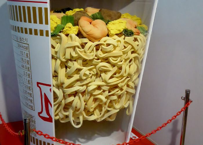 A close up image of a display at the Cup Noodles Museum, showing a huge model of a pot of cup noodles cut open to display what's inside