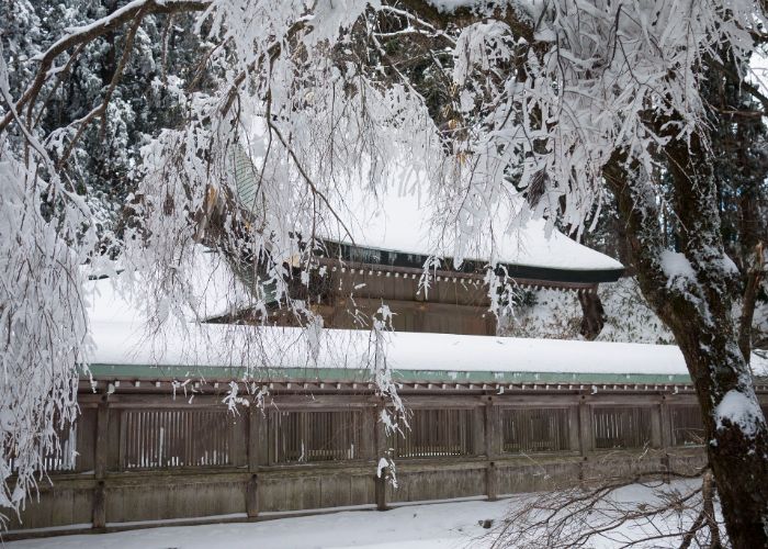 A wooden temple building covered in snow, with ice-covered trees in the foreground