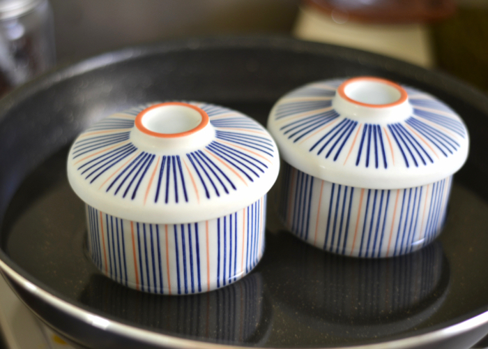 Two covered chawanmushi cups steaming in a pan of water