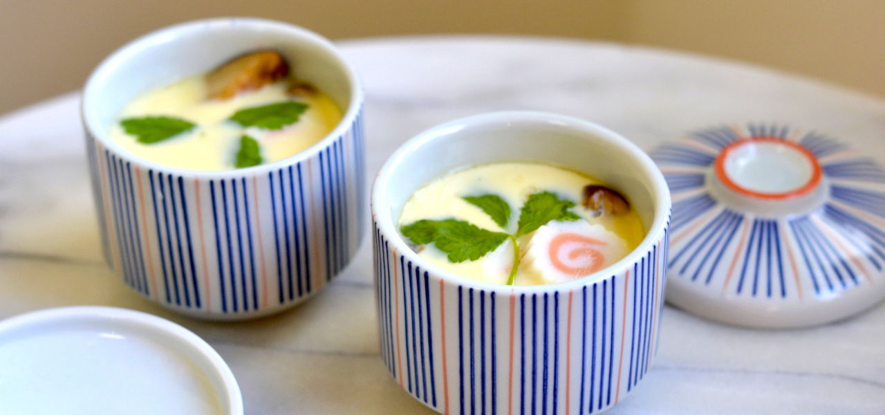 Two cups of chawanmushi with vibrant garnish on a marble surface