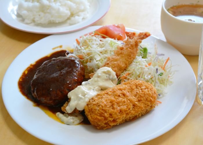 A plate with cabbage salad and a variety of yoshoku dishes like ebifry, corokke, and hamburger