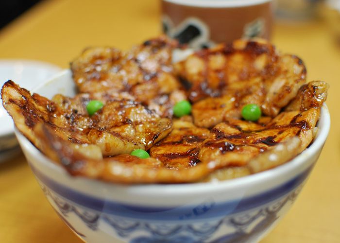 A close up image of a bowl of butadon, topped with thick slices of pork