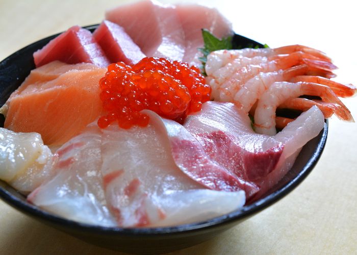 A close up of a bowl of kaisendon, topped with slices of fish and prawns