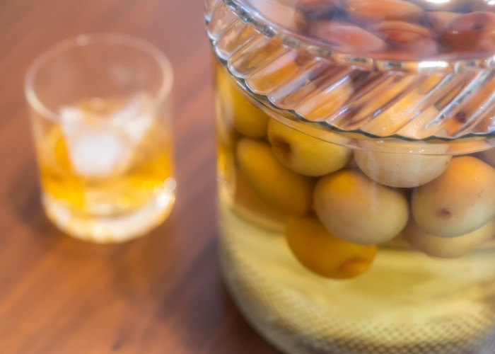 A jar of Japanese plum liquor on a table with a glass of plum liquor in the background.