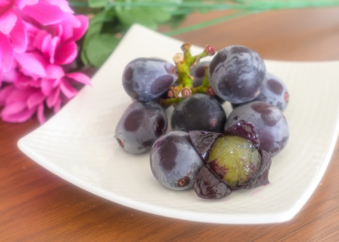 Kyoho brand grapes on a plate. One is peeled to reveal the flesh inside.