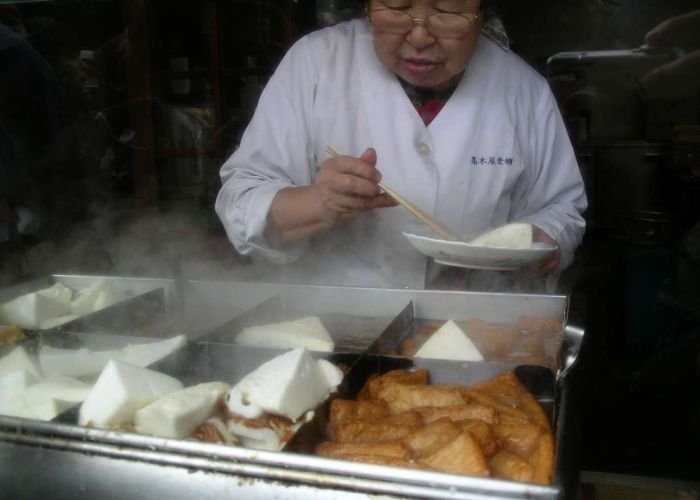 An elderly street vendor serving hanpen and fishcake oden