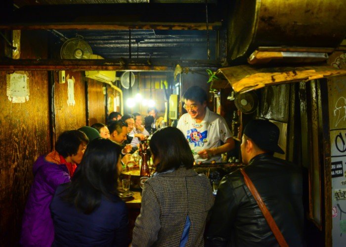 people crowded around a counter in an old izakaya
