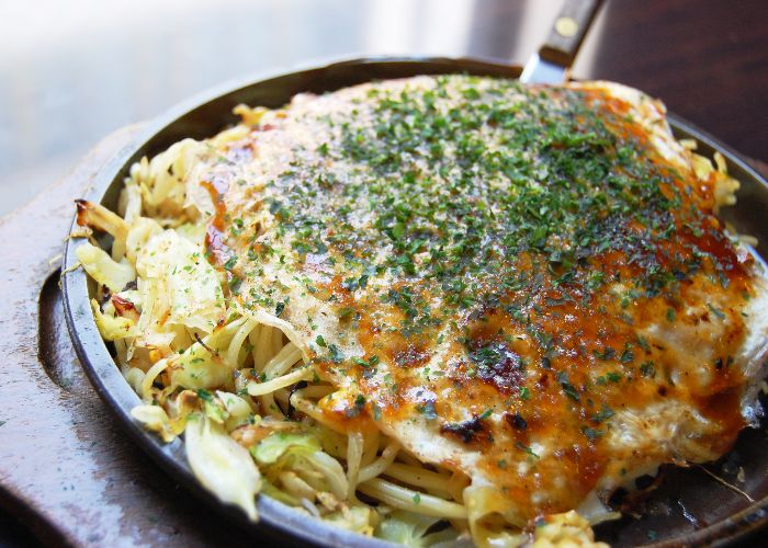 A close-up image of okonomiyaki, topped with dark green flakes of seaweed