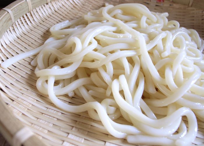 A close-up shot of fresh, plain white udon noodles on a bamboo basket