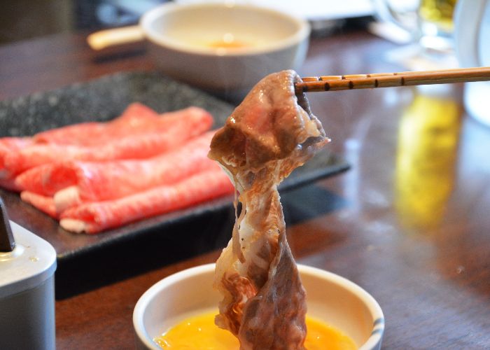 Cooked meat being dipped in egg for sukiyaki
