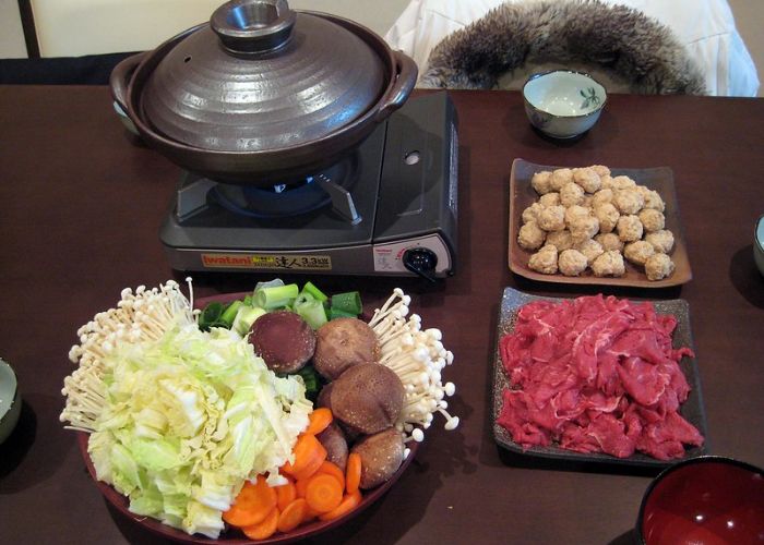 A table with all the materials needed to make nabe, the pot, vegetables, and meat