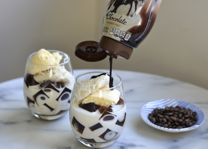 Chocolate syrup being poured over a glass of coffee jelly