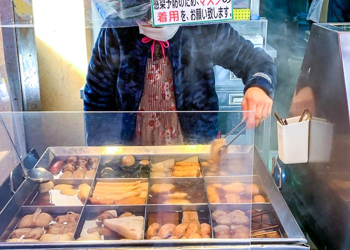 A lady serves oden from a variety of oden holders
