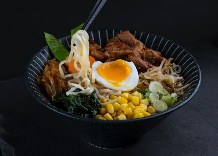 Bowl of ramen with lots of vegetables on a black background