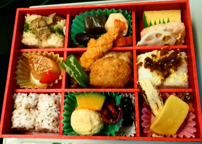 Red bento box with different compartments filled with food on a shinkansen train