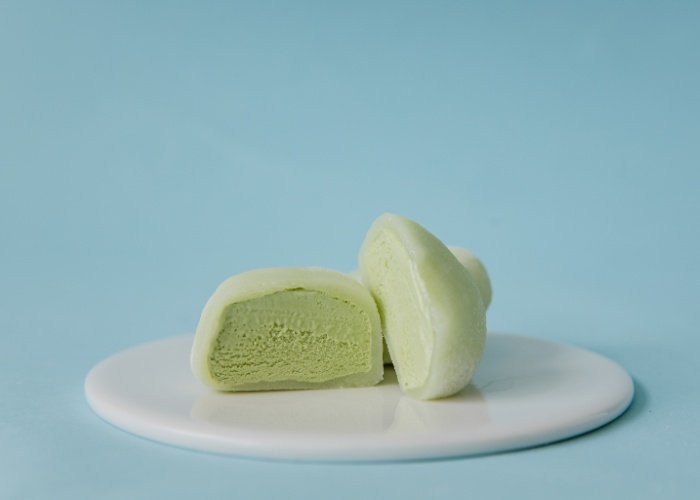 Green tea ice cream mochi on a white plate with a blue background