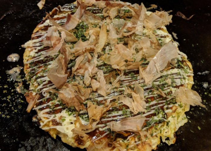 Okonomiyaki savory pancake on a grill with mayo and katsuobushi on top