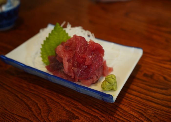 A ball of chopped tuna sashimi sits next to a mound of wasabi, shredded daikon and a shiso leaf