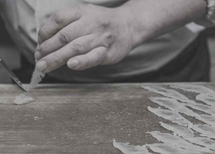 grayscale hands thinly slicing a light fleshed fish for sashimi